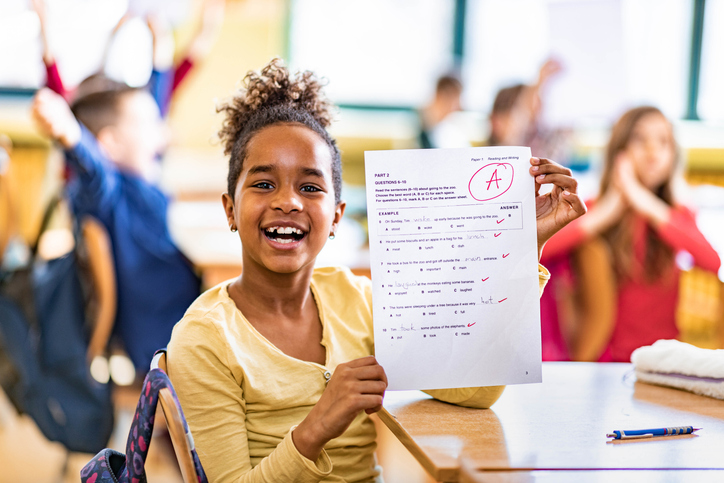 Happy African American schoolgirl showing her A grade on a test at elementary school and looking at camera. for article on spaced learning