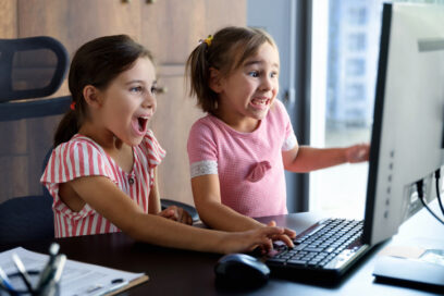 Image of two young girls facing to the right, appearing exciting as they look at a computer screen. Image used for SmartBrief Technology story headlined: Securing the digital playground: How AI can protect children in online gaming