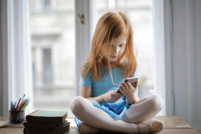 Sad or studious-looking girl in blue shirt sitting cross-legged and touching smartphone for education story on math anxiety