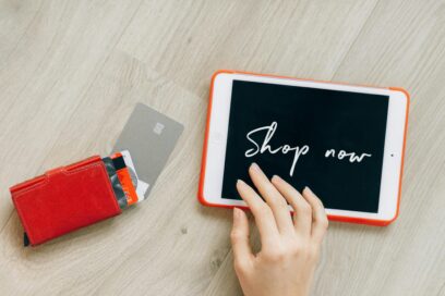 An image of a small iPad-like device with a right hand on it, and "shop now" on the screen. To the left is what looks like a small wallet with a credit card sticking out. Image used for a SmartBrief story entitled, What’s trending in media retail networks